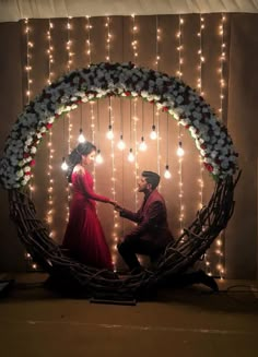 a man kneeling down next to a woman in front of a wreath with lights on it