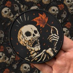 a hand holding a black and orange patch with a skeleton on it's back