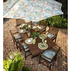 an outdoor dining table set with plates and utensils under an umbrella on a brick patio