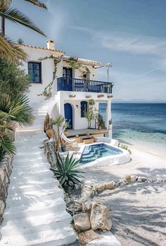 a white house with blue shutters next to the ocean and palm trees in front of it