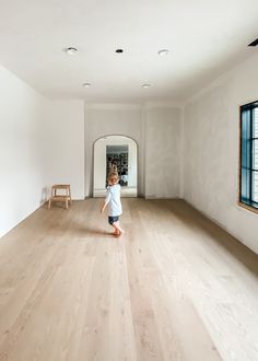 a little boy standing in the middle of an empty room with wooden floors and white walls