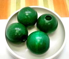 three green wooden beads sitting in a white bowl on a striped tableclothed surface