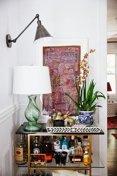 a table with vases and plants on it in front of a wall hanging tapestry