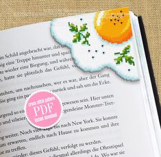 cross stitch bookmark with an orange on the cover and text in german that reads,