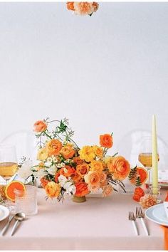 an orange and white table setting with flowers in vases on the centerpiece, silverware and candlesticks