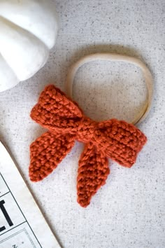 an orange crocheted bow on a wooden headband next to a white pumpkin