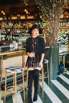 a woman standing in front of a bar wearing black boots and a dress with stripes