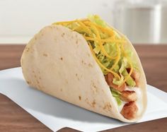 a tortilla with chicken, lettuce and cheese on it sitting on top of a piece of paper