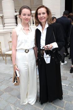 two women standing next to each other in front of a white building with columns and pillars