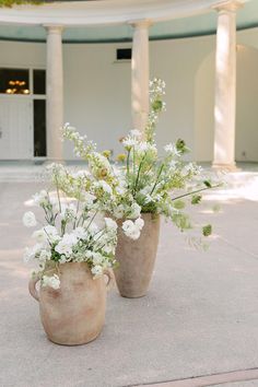 two vases filled with white flowers sitting on top of a cement floor next to columns