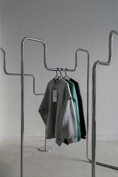 three sweaters hanging on clothes racks in an empty room