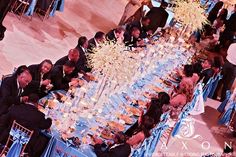 a group of people sitting around a table with blue clothed tables and chairs in front of them