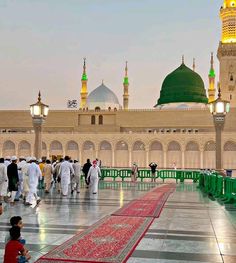 many people are walking around in front of a building with green domes and yellow lights