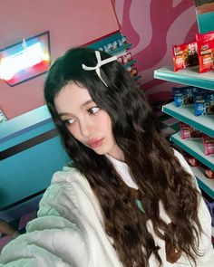 a girl with long dark hair is standing in front of a store shelf and looking at the camera