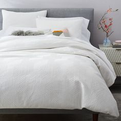 a bed with white and grey comforter next to a night stand in a bedroom