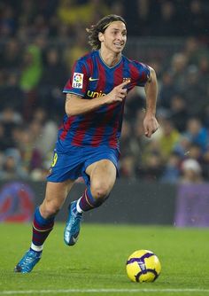 a soccer player is running with the ball in front of him and people watching from the stands