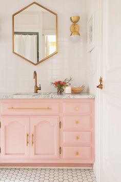 a bathroom with pink vanity, gold mirror and hexagonal tiles on the floor