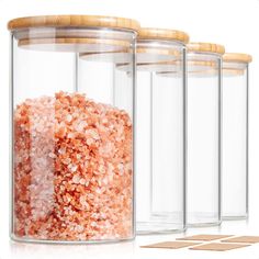 three glass containers with wooden lids filled with pink and white sugar cubes next to each other