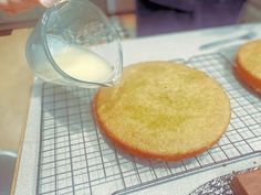 a person pouring milk into a cake on a cooling rack next to other pastries