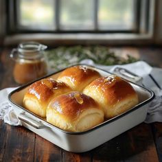 four rolls in a pan on a wooden table next to a jar of peanut butter