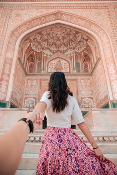 a woman holding the hand of a man in front of an ornate building with arches and doorways