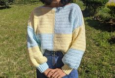 a woman standing in the grass wearing a yellow and blue sweater