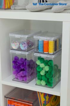 three clear storage bins filled with different colored balls and sprinkles on top of a white shelf