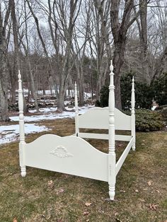 a white bed sitting on top of a lush green field covered in snow next to trees