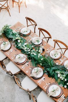 the table is set with white plates and greenery