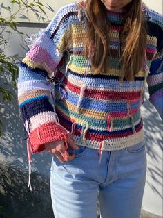 a woman wearing a multicolored crocheted sweater and jeans with her hands in her pockets