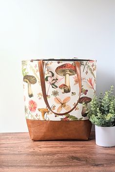 "This tote bag is a great bag to carry every day.  Use it for work, school, shopping, or even as a stylish diaper bag. Mushroom Garden Tote: Fungi and Floral, Vegan Leather Tote, Work Bag ~This bag is made of gorgeous twill fabric featuring various mushrooms and florals on a white background.  ~The bag is reinforced with heavy interfacing, adding extra durability and shape while still being light weight.   ~The base part is made of high-quality faux leather in nice warm toffee brown. ~Heavy black canvas fabric lining with one zipper pocket, perfect for keys, phone, and accessories.  There is a gold magnetic snap to help keep the bag closed and secure.  ~Straps are made of matching vegan leather fixed with two gold rivets for extra strength.  Approximate Measurements: Height: 14.5\" Width(o Everyday Beige Shoulder Bag For Gifts, Canvas Tote Bag With Removable Pouch, Large Capacity Tote Diaper Bag For Errands, Everyday Bucket Canvas Bag With Handles, Everyday Leather Tote Diaper Bag, Leather Tote Diaper Bag For Daily Use, Brown Everyday Bag Suitable For Gifts, Canvas Tote Bag As Gift Bag For Errands, Daily Use Canvas Pouch Bag With Leather Handles