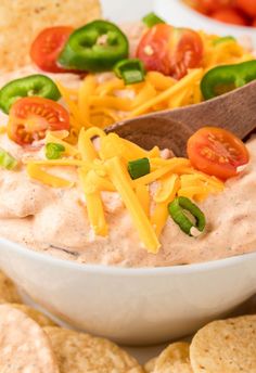 a white bowl filled with dip surrounded by crackers and tomatoes