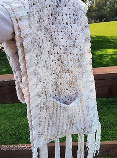 a white crocheted shawl hanging from a wooden fence in front of grass