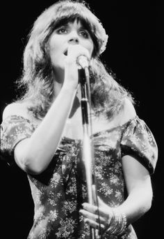 a woman holding a microphone in front of her face and wearing a dress with flowers on it