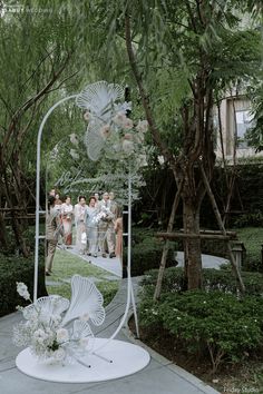 a group of people standing in front of a white sculpture with flowers and umbrellas on it