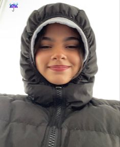 a young boy wearing a black jacket and hood smiling at the camera with his eyes closed