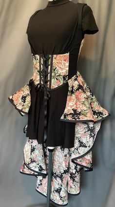 The under bust vest, meticulously tailored to accentuate your curves, offers a flattering silhouette. Its intricate floral design, reminiscent of the lush gardens of old-world estates, adds a touch of ethereal charm to your attire. The flowing fabric, adorned with delicate blooms and verdant foliage, lends an air of whimsy and sophistication to your ensemble. The outer fabric is a cotton blend and it is lined with a strong duck canvas. Spiral steel boning is encased in the seams and straight met Sleeveless Fitted Corset Dress For Garden Party, Fitted Floral Print Corset Dress For Garden Party, Floral Print Fitted Sleeveless Corset, Fitted Feminine Floral Print Corset Dress, Fitted Overbust Corset Dress With Floral Print, Fitted Overbust Dress For Garden Party, Floral Sleeveless Corset Dress With Fitted Bodice, Garden Party Overbust Corset Dress, Floral Print Overbust Corset With Fitted Bodice