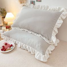 a white bed with two pillows and a plate of fruit on the floor next to it