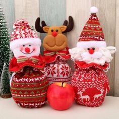 three christmas ornaments sitting on top of a table next to an apple and santa clause