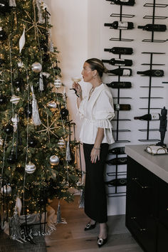 a woman standing in front of a christmas tree holding a wine glass and looking up