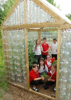 a group of children standing in front of a small greenhouse