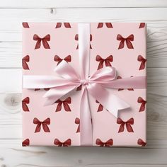 a pink gift box with red bows and ribbon on white wooden background, top view