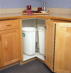 two trash cans sitting in the corner of a kitchen cabinet with their lids down and one is open