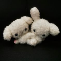 two small white teddy bears sitting next to each other on a black surface with one holding the other's hand