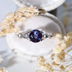 a ring with a blue stone in it sitting on top of a white box next to dried flowers