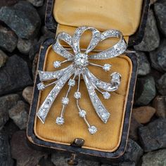 This 14k white gold diamond brooch features a ribbon design and is bordered with milgrain edging. The brooch is centered with one (1) round brilliant cut diamond set into a six-prong setting. The brooch is also accented with forty-four (44), bead/prong set, round brilliant/single cut diamonds. The brooch measures 43.6mm X 31.0mm. Classic Platinum Brooch With Brilliant Cut, Vintage Brooches With Brilliant Cut Diamonds, Classic Platinum Brooches With Diamond Accents, Art Deco White Gold Diamond Brooch, Classic Round Diamond Brooches, Luxury Diamond White Brooch With Brilliant Cut, Classic Diamond Brooch, Classic Diamond White Brooch For Anniversary, Classic Diamond White Brooches For Anniversary