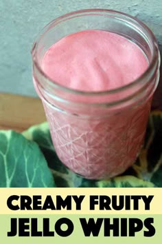 a jar filled with pink jello sitting on top of a green leaf covered table