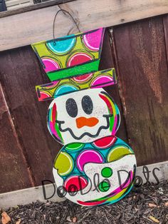 a painted snowman sitting on the ground next to a wooden fence