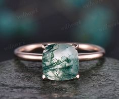 a ring with a green and white stone on it sitting on top of a rock