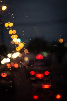 rain drops on the windshield of a car as traffic lights shine brightly in the background